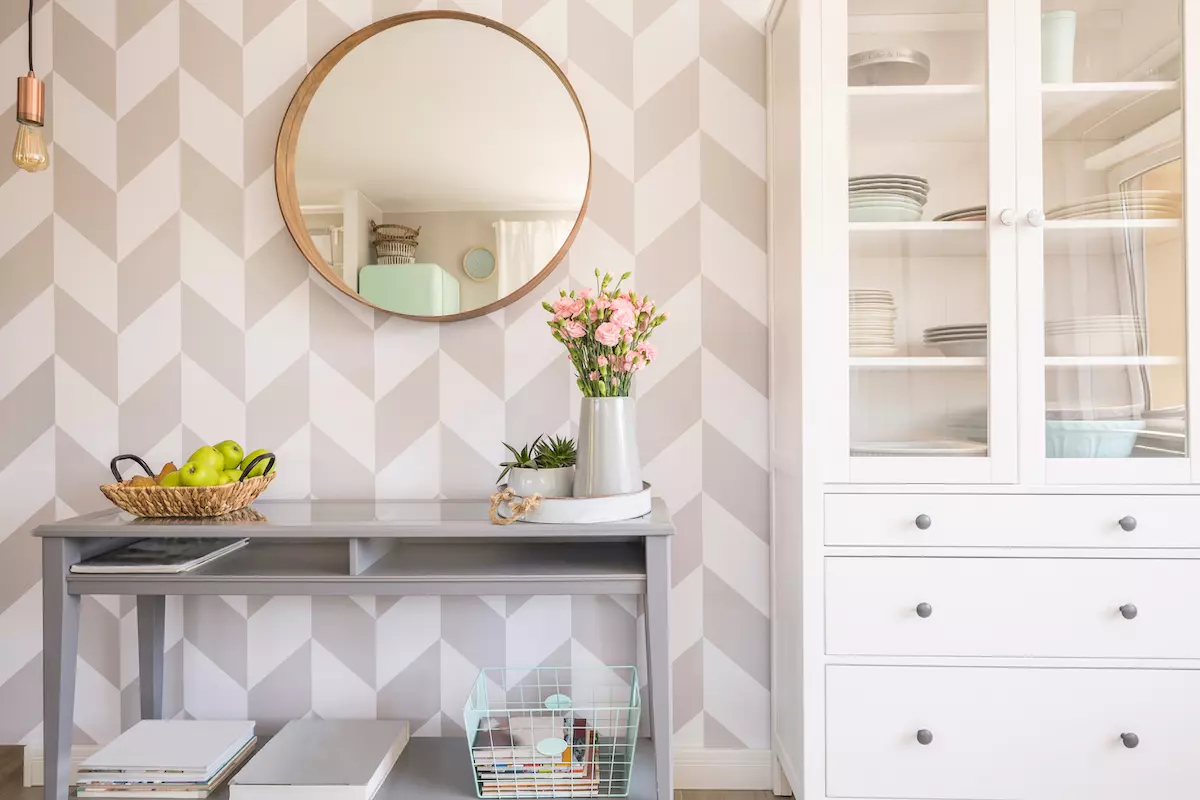 Mirror on patterned wallpaper above grey table with flowers