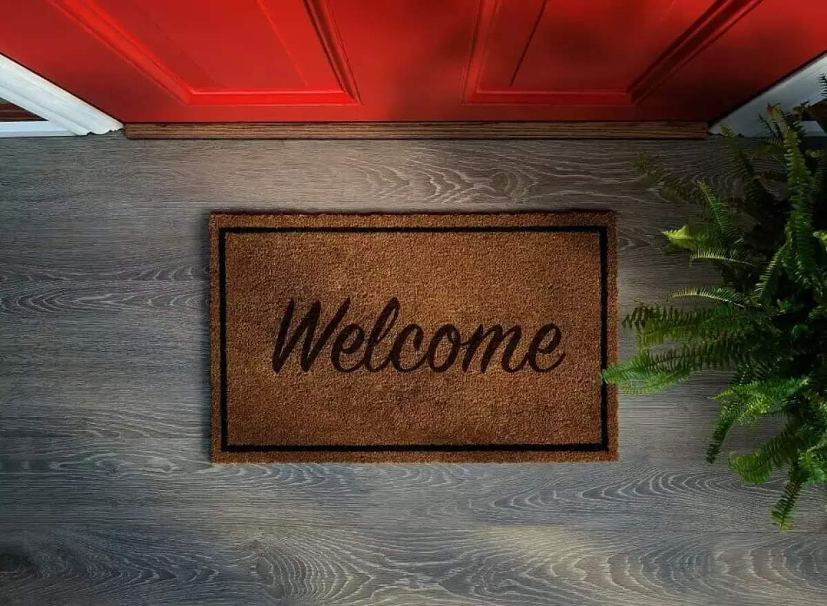 A welcome doormat outside a red front door of a home
