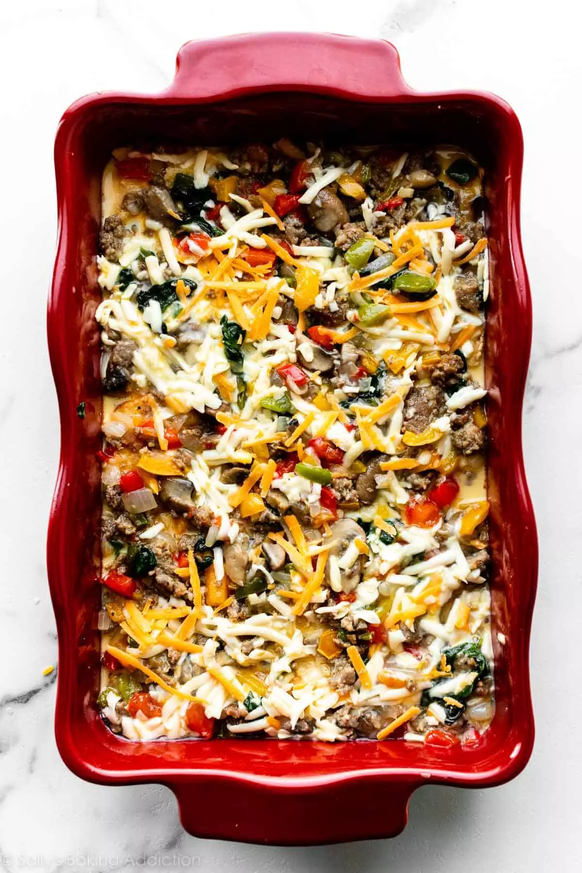 egg, vegetables, cheese, sausage, and bread combination in a casserole dish on a marble counter.