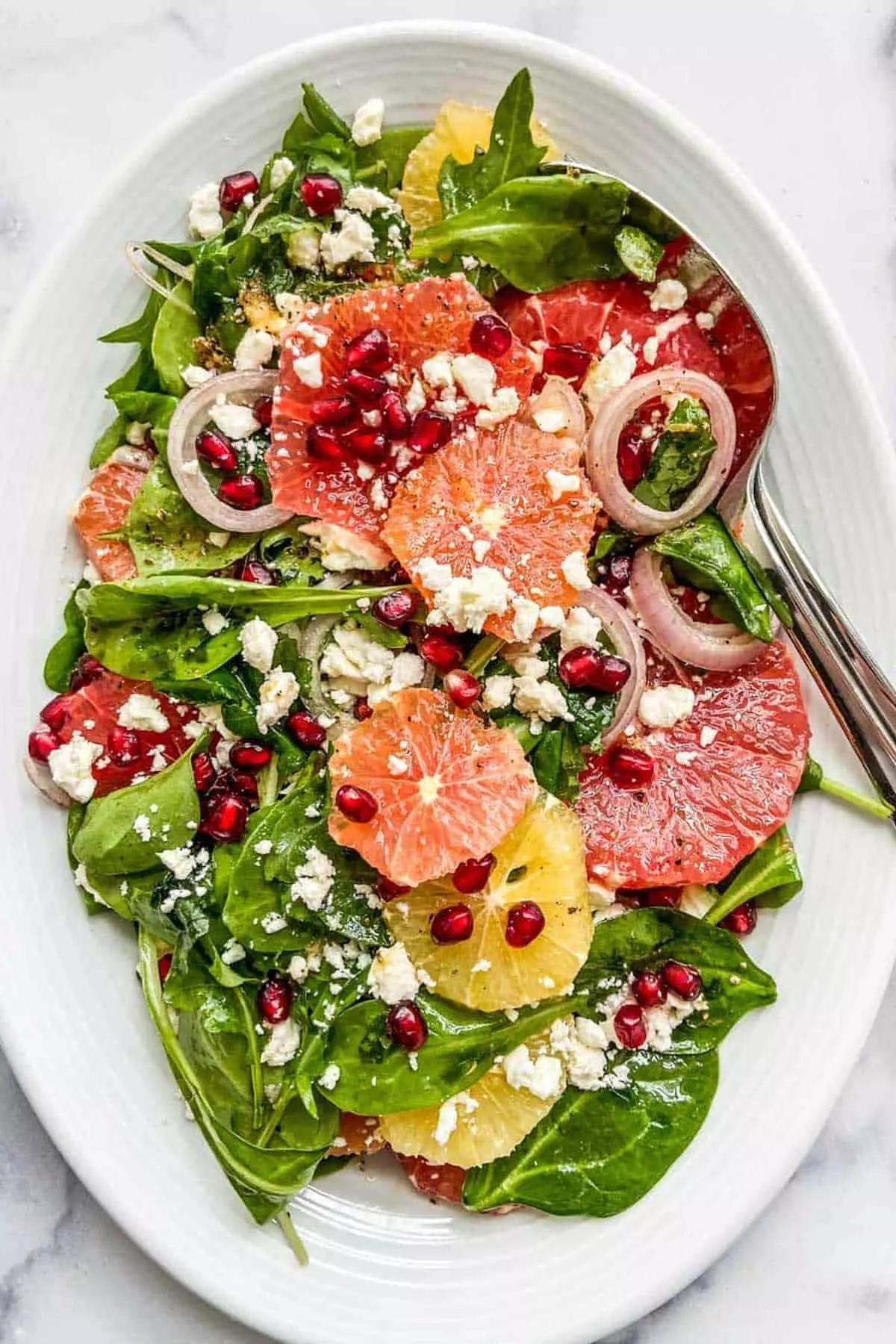 A citrus pomegranate salad with feta cheese on a white platter.