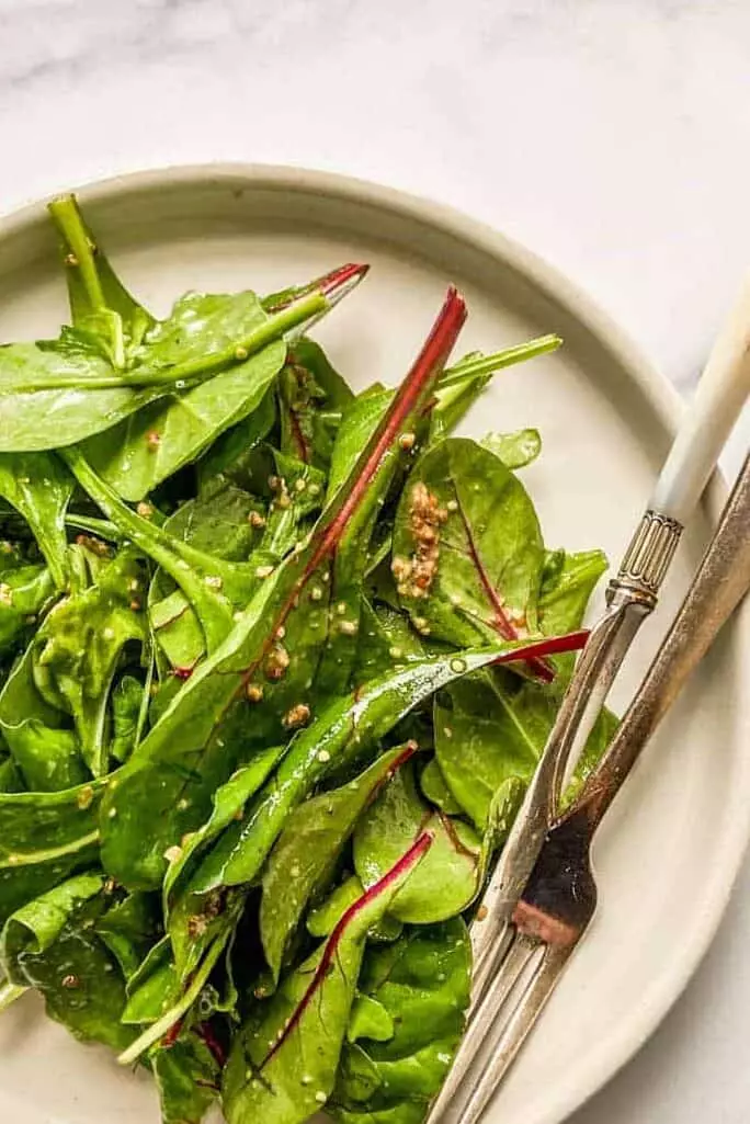 A simple green salad on a white plate with a fork and a knife.