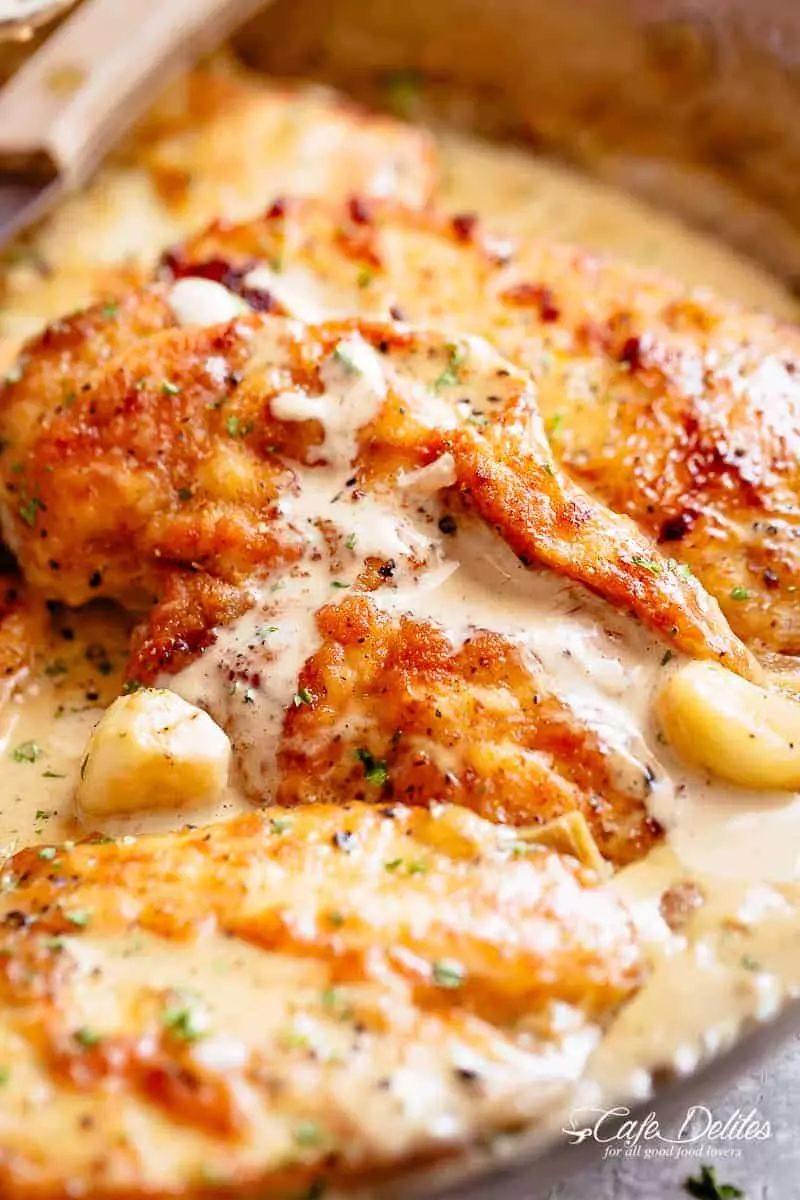 Chicken breasts are pan-fried until golden and crispy before being added to a mouth-watering garlic cream sauce! A silver fork pierces through a sliced piece of chicken! | cafedelites.com