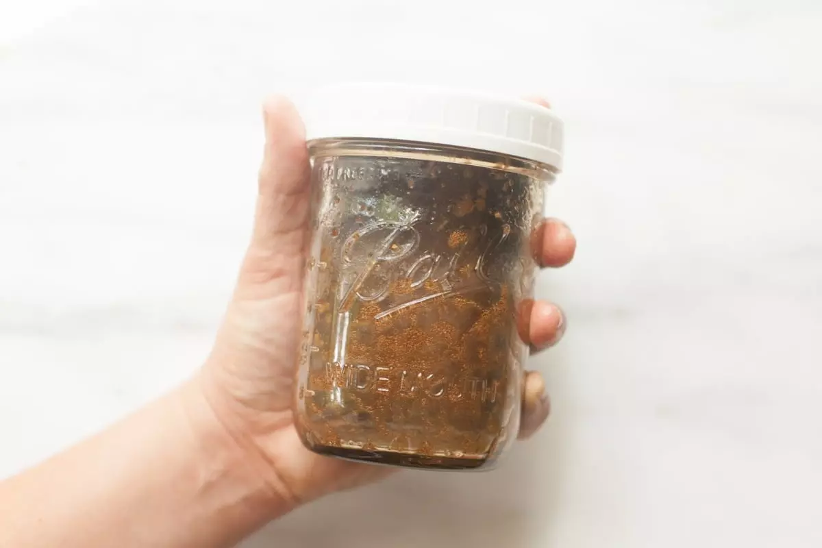 A hand holds out a half pint mason jar filled with balsamic vinaigrette