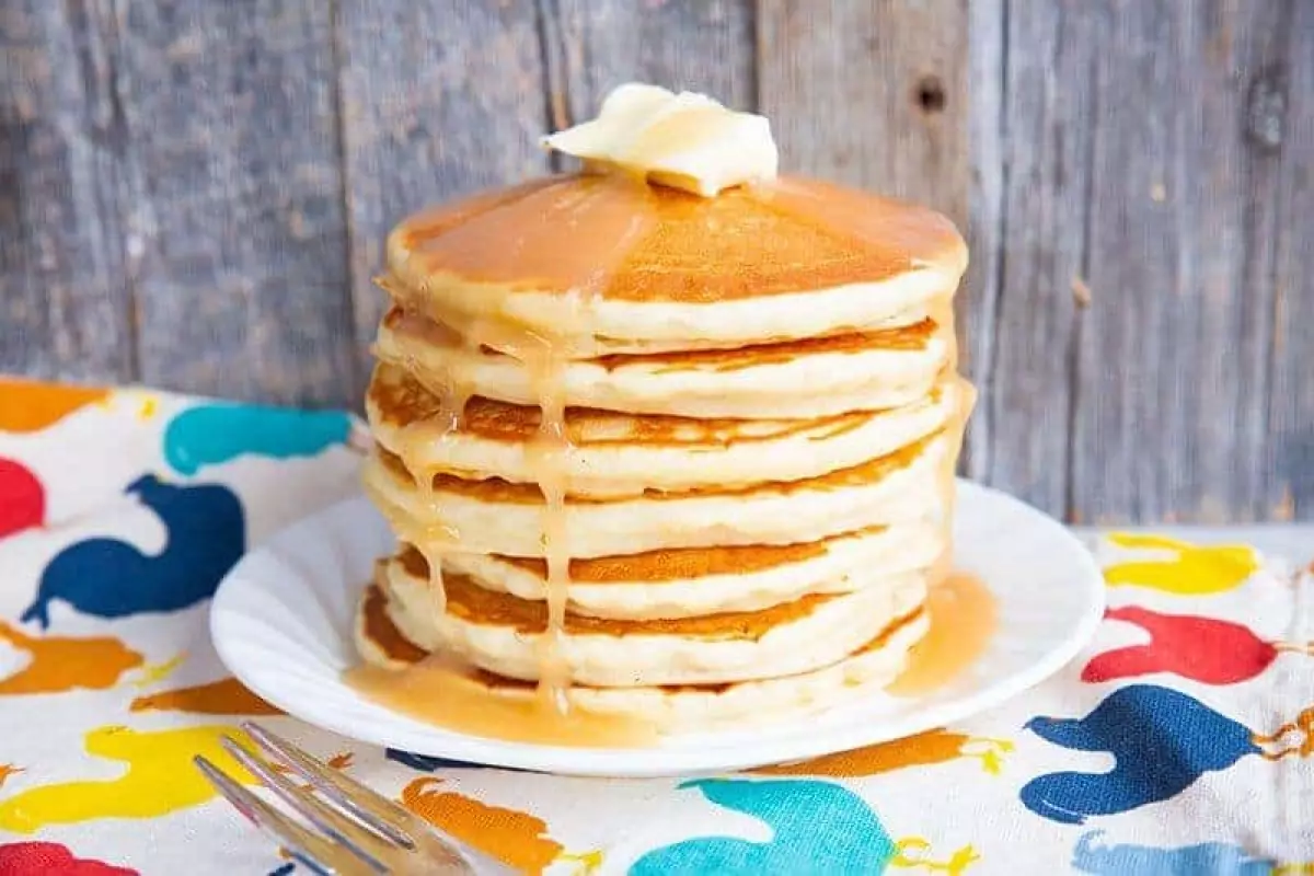 A stack of pancakes on a white plate with butter and syrup on top